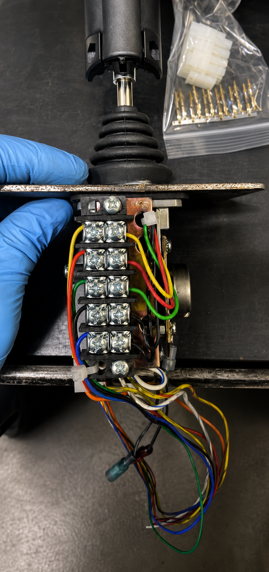 Technician in a blue glove holding a control joystick assembly with terminal block connections and multi-colored electrical wiring
